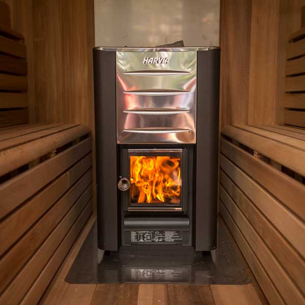 Front view of a wood-burning sauna heater showcasing its sleek design and chimney, with logs in the firebox and a metallic finish, set against a wooden sauna backdrop.