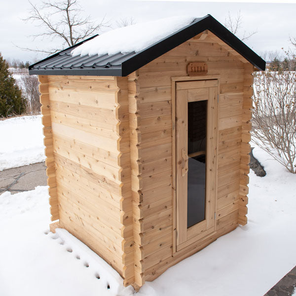 Front door and left side view of the Granby Cabin Sauna, with a roof covered in snow.