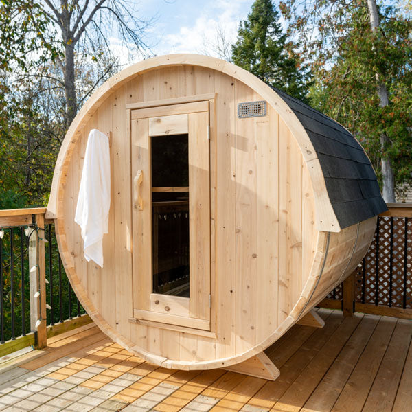 Front view of a Harmony Barrel Sauna with an open glass door, surrounded by trees.