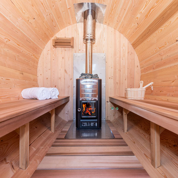 Inside view of a Harmony Barrel Sauna featuring a sauna heater with a flue pipe in the center and two benches on each side.