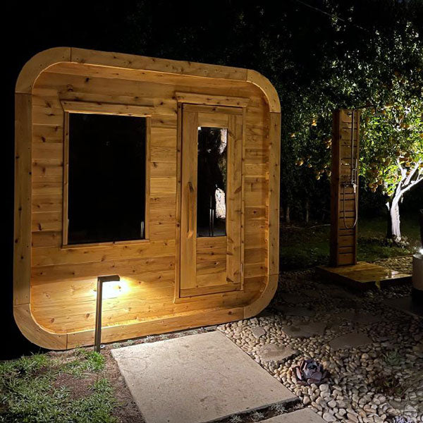 Front view of a Canadian Timber Luna Sauna with a glass window and door at night.
