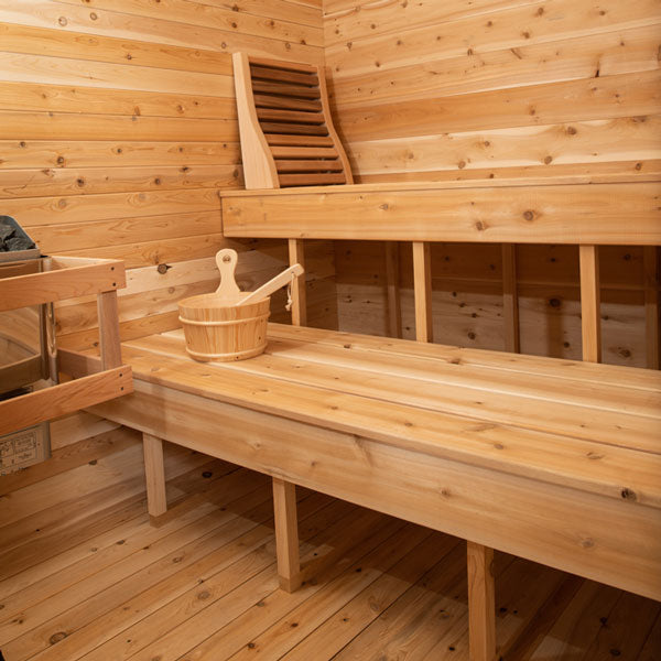 Inside view of a Canadian Timber Luna Sauna, featuring a sauna heater on one side, two benches, and additional accessories.