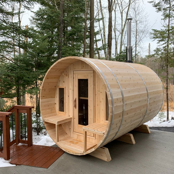 Front and right side view of a tranquility barrel sauna with a porch, glass windows, and doors, positioned next to stairs.