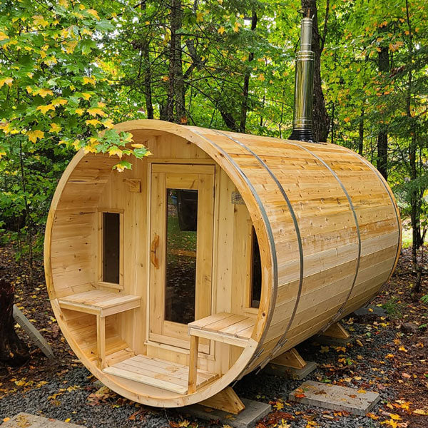 Front and right side view of a tranquility barrel sauna with a porch, glass windows, and doors, surrounded by trees.