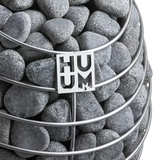 Close-up view of the HUUM Drop electric sauna heater highlighting its stainless steel finish and sauna rocks.