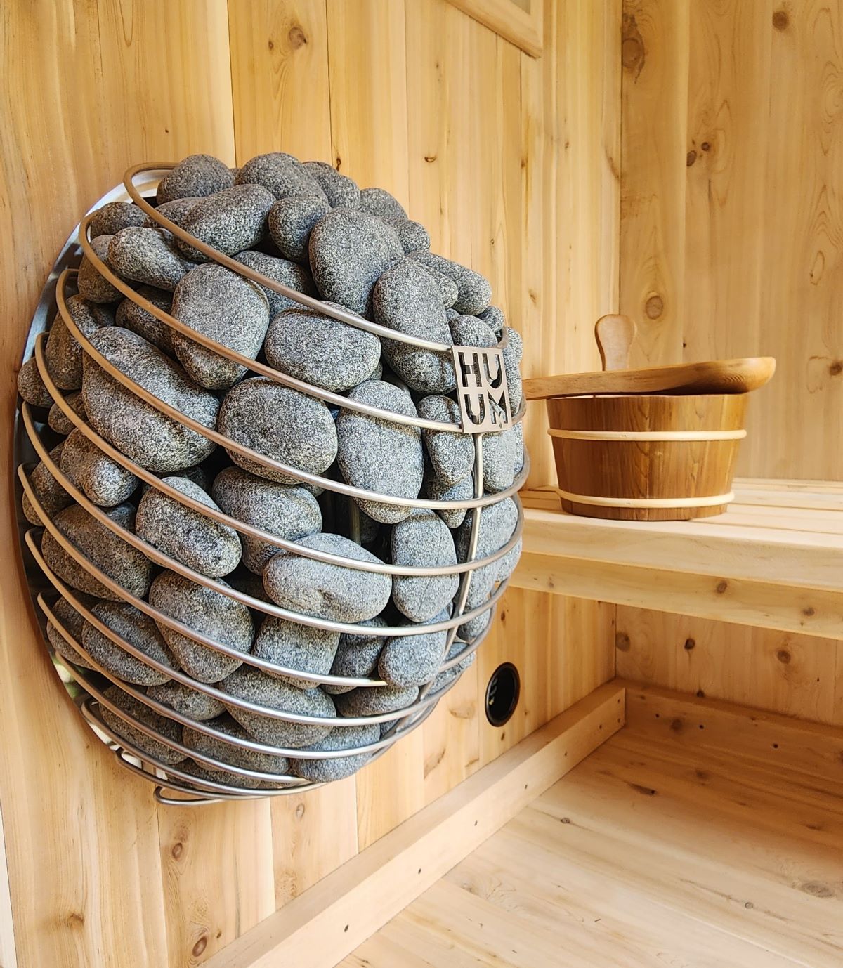 Side view of the HUUM Drop 9KW electric sauna heater mounted on a wooden wall, highlighting its stainless steel finish and sauna stones.