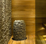 Huum Hive  Mini sauna heater model HIVE Mini , displayed in a wooden cabin adjacent to a rock wall, highlighting its compact design in a rustic environment.