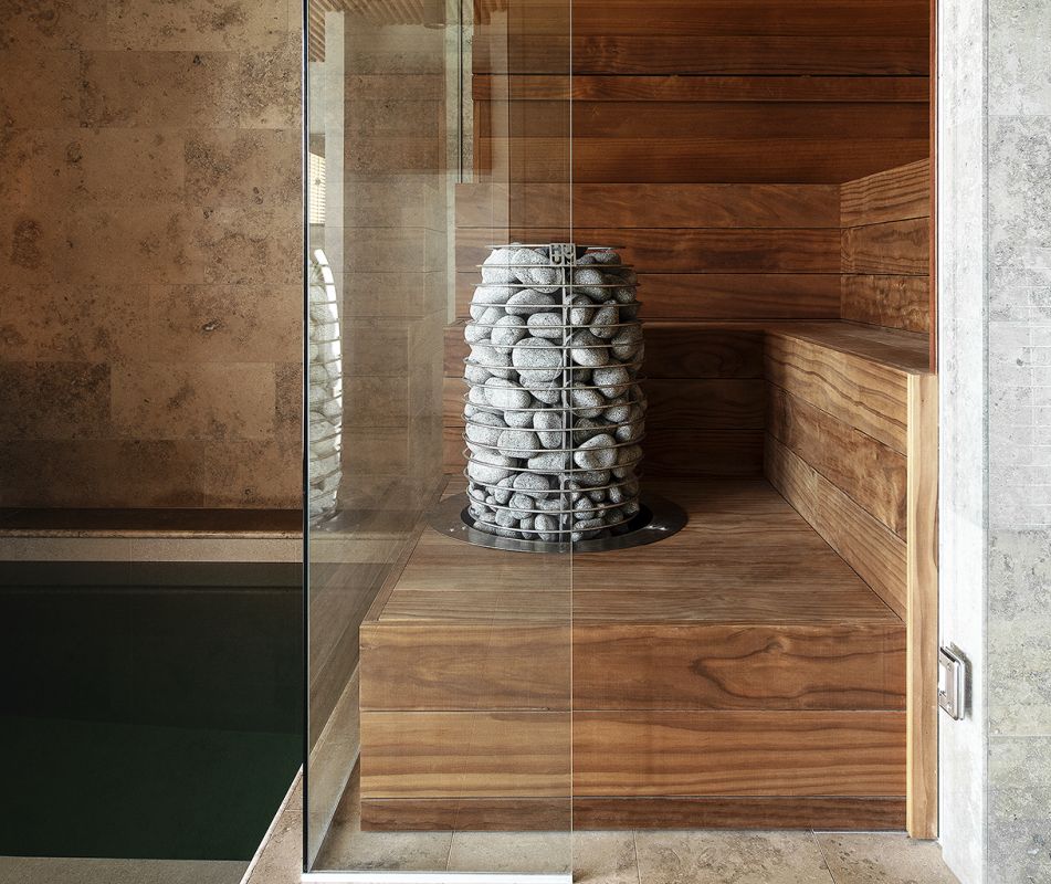 Huum Hive Mini sauna heater model HIVE Mini , located in a wooden cabin featuring a glass wall divider, highlighting its sleek design in a contemporary setting.