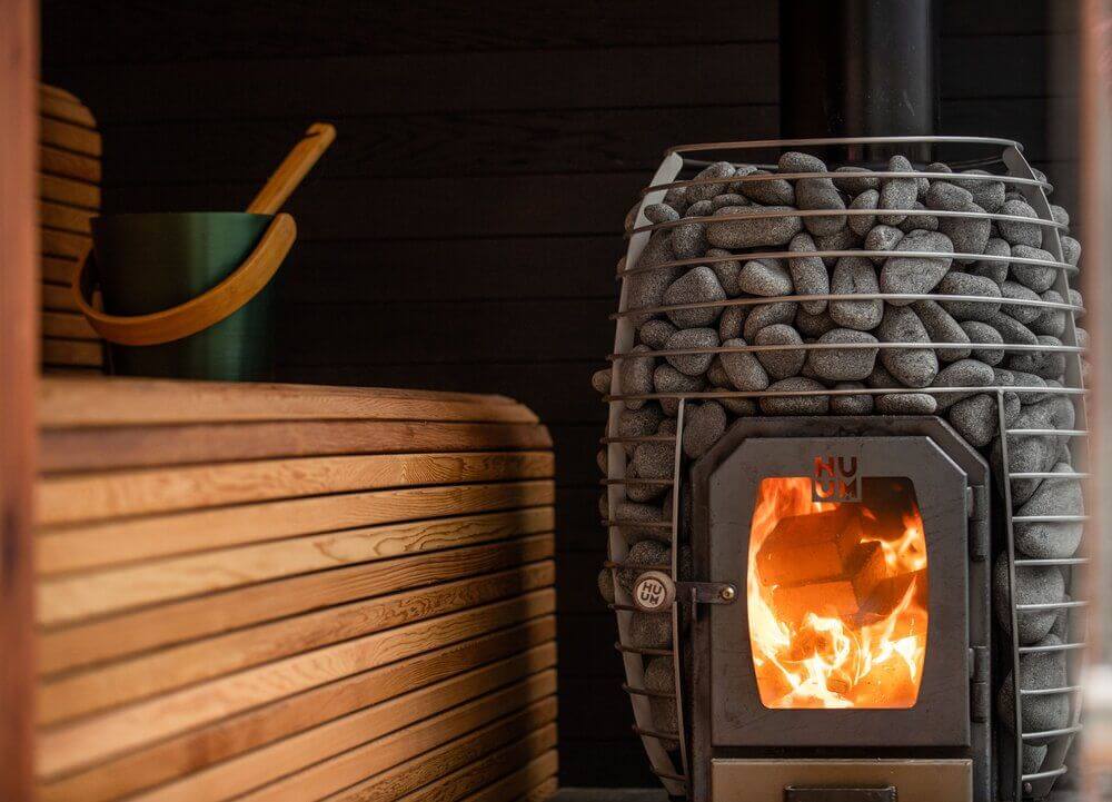 Wood burning inside a Huum wood heater, with rocks positioned on top for added insulation.