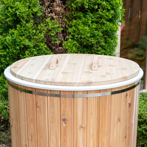A round cold plunge tub covered with a protective lid. The tub features a smooth surface and is surrounded by a natural setting, emphasizing its functional design and outdoor suitability.